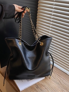 Minimalist black tote bag with woven chain strap on dark wood surface in soft lighting