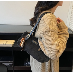 Close-up of black matte suede shoulder bag with colorful wooden bead tassel and gold logo