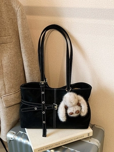 Bolso tote retro negro con costuras blancas y colgante de conejo sobre una maleta