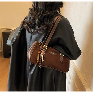 Close-up of a dark brown suede baguette bag with vintage bead charm and metal logo