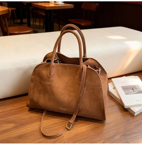 Detail of caramel suede tote bag with gold logo and dual leather handles in coffee shop
