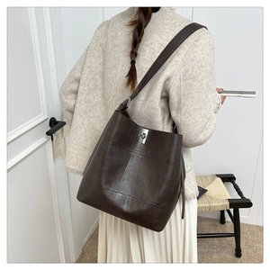 Detailed view of the dark brown leather bucket bag with silver buckle worn by a model
