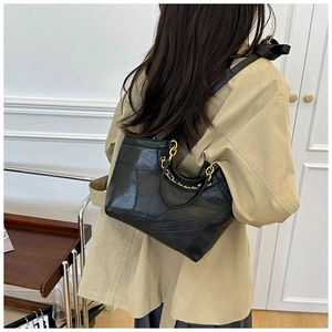 Dettaglio borsa a secchiello in pelle PU nera con catena oro su un trench coat