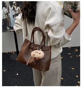 Close-up of brown PU leather tote bag with a beige plush doll charm in outdoor setting