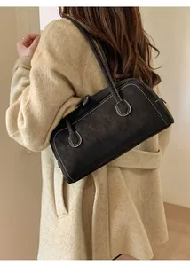 Détail du sac sous le bras en daim noir avec surpiqûres sur une tenue de manteau beige