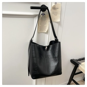 Detail of black pebbled leather bucket bag with silver metal buckle hanging on wall