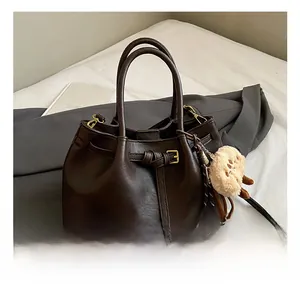 Deep brown matte leather bucket bag featuring a white alpaca plush charm and buckle detail