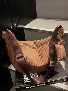 Brown pleated hobo bag with wide strap and matching small pouch on a modern urban background