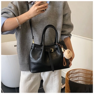 Detail view of black matte handbag with gold buckle, round handles and plush charm