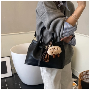 Detail of black leather bucket bag with decorative strap and plush sheep charm on model