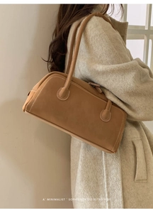 Détail du sac bandoulière en daim marron avec coutures blanches sur un manteau