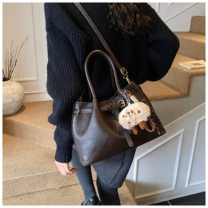 Detail of dark brown pebble leather tote bag with metal buckle and plush animal charm