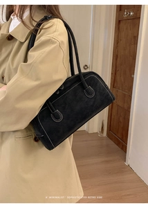 Détail d'un sac baguette noir en daim avec surpiqûres porté sur un trench-coat beige