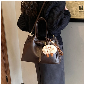 Detail of dark brown leather tote bag with plush sheep charm and adjustable strap