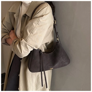 Detail view of a vintage dark brown leather hobo bag with fringe on a beige trench coat