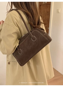 Détail d'un sac à bandoulière en daim marron avec surpiqûres blanches et fermeture éclair