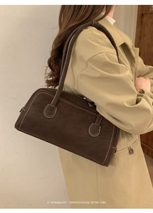 Détail du sac à main en daim marron foncé avec surpiqûres blanches et fines poignées