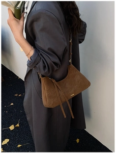 Detail of dark brown suede shoulder bag with tassel and gold hardware in autumn setting