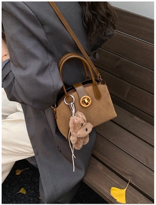 Detail of suede shell bag with golden ring clasp and plush puppy charm in autumn setting