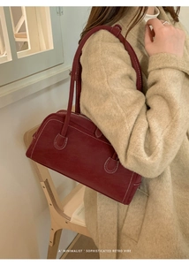 Détail du sac rétro bordeaux avec surpiqûres blanches porté sur un manteau beige