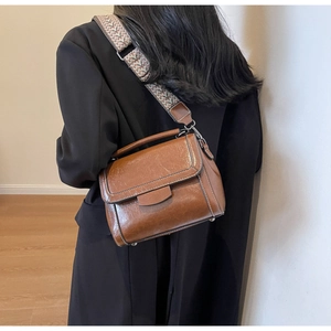Close-up of retro brown messenger bag featuring patterned wide strap and polished hardware