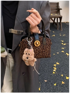 Close-up of leopard print handbag with gold twist lock and brown plush dog charm