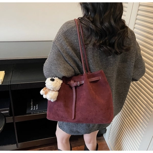Dettaglio borsa tote bordeaux opaca con fibbia decorativa e ciondolo a forma di orsetto