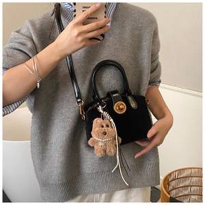 Detail of a black mini handbag with gold twist lock and a cute plush bear charm