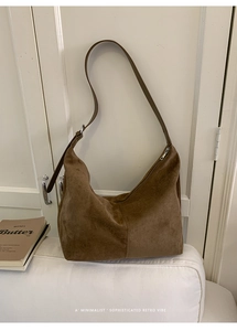 Detail of minimalist brown suede hobo bag with stitching on a cozy white sofa background