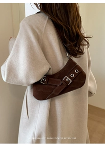 Close-up of retro brown suede underarm bag with decorative metal buckles and eyelets