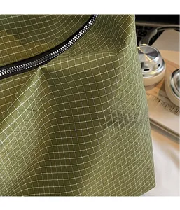 Detail of green plaid tear-resistant fabric and smooth black metal zipper on tote bag