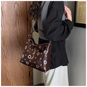 Détail du sac cabas en cuir verni marron foncé avec œillets métalliques argentés