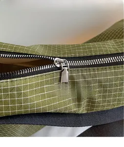 Close-up of a smooth silver metal zipper on an olive green checkered tote bag fabric