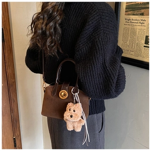 Close-up of vintage brown suede shell bag with golden metal lock and plush dog charm