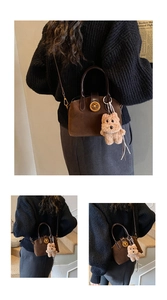 Detail view of brown suede shell bag with gold buckle and cute plush bear charm