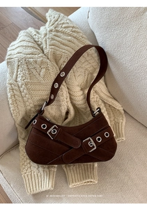 Détail d'un sac à bandoulière en daim marron foncé avec anneaux en métal sur un tricot