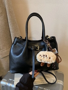 Chic black PU leather tote bag with gold buckle, plush charm, and long strap on luggage