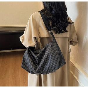 Black plaid tote bag shown on a model in a cozy trench coat within a modern home