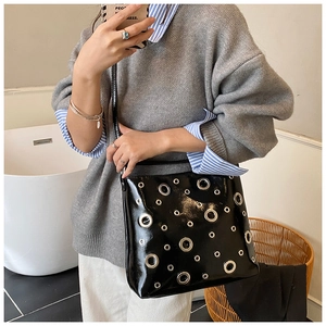 Détail du sac bandoulière en cuir verni noir brillant avec œillets métalliques argentés