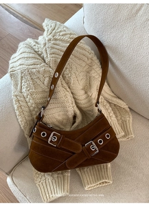 Détail d'un sac d'épaule en daim marron foncé avec boucles argentées sur un pull en maille