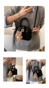 Detail of black mini shell bag with golden twist lock and cute plush puppy charm pendant