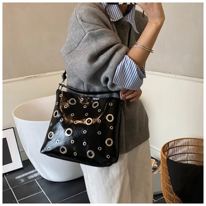 Détail du sac à bandoulière en cuir verni noir avec œillets métalliques style punk