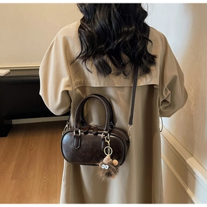 Detail der dunkelbraunen Vintage-Boston-Tasche mit Plüschanhänger und schmalem Gurt
