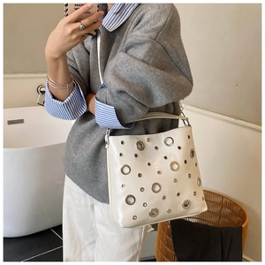 Détail d'un sac à bandoulière blanc avec œillets métalliques argentés et design moderne