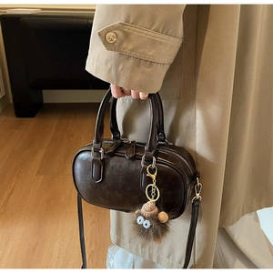 Detailansicht der dunkelbraunen Zylinder-Handtasche mit Plüsch-Anhänger und Reißverschluss