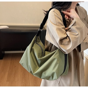 Detailed shot of green checkered tote bag with adjustable black strap on casual trench coat
