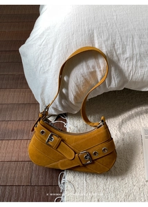 Détail du sac sous le bras en daim jaune moutarde avec boucle en métal sur fond doux