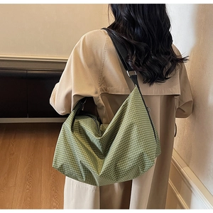 Detail of a large green grid tote bag showing adjustable black strap on a khaki trench coat