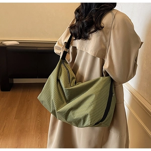 Detail of green plaid canvas tote bag worn over a trench coat for daily casual commute