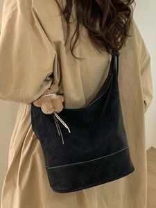 Large black suede bucket bag with bear charm worn by a model in a camel coat